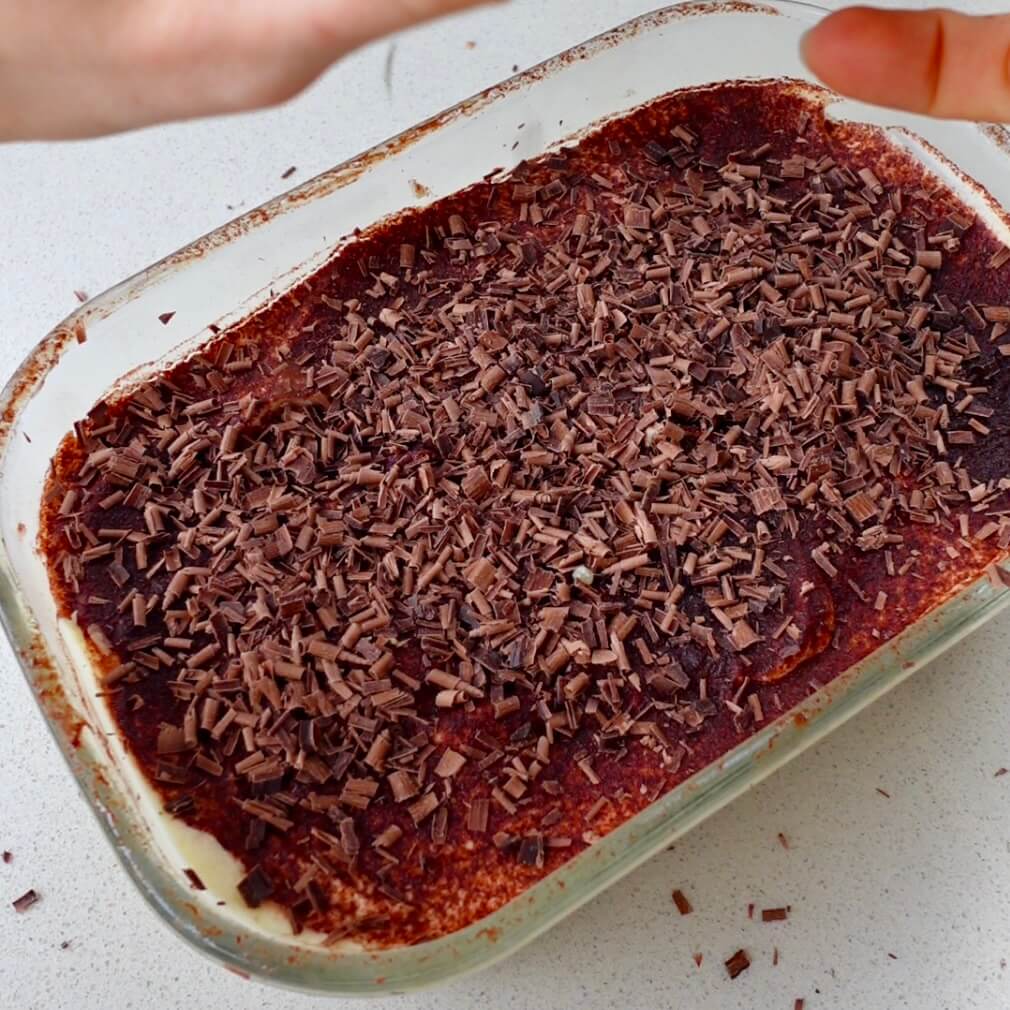 a glass baking dish filled with tiramisu topped with shaved chocolate